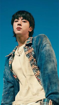 a young man with black hair wearing a blue jacket and white t - shirt standing in front of a blue sky