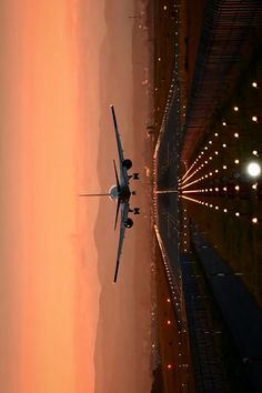 an airplane is flying over the water at sunset or sunrise with lights in the background