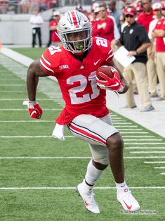 a football player running with the ball in his hand and people watching from the sidelines