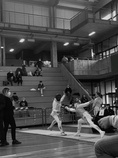 some people are playing baseball in an indoor arena with stairs and railings, while others watch from the bleachers