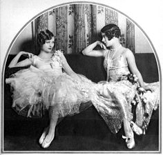 two women in dresses sitting on a couch