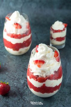 two desserts with strawberries and whipped cream in them on a blue surface next to some strawberries