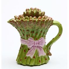 a green vase with pink flowers and a bow on the handle is sitting in front of a white background