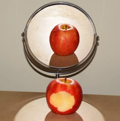 an apple sitting in front of a mirror on top of a table with its reflection