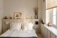 a bed with white linens and pillows in a bedroom next to a window filled with vases