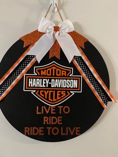 a harley davidson sign hanging on the wall with ribbon around it's edge and an orange bow at the top