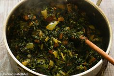 a pot filled with cooked vegetables on top of a wooden table next to a spoon