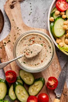 a jar filled with dressing next to a bowl of cucumbers, tomatoes and chickpeas