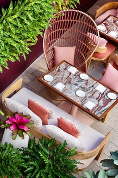 an outdoor seating area with pink cushions and pillows on the table, surrounded by greenery