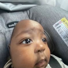 a baby in a car seat looking at the camera with an alert sticker on his head