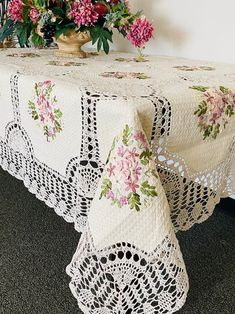 a white table with pink flowers in a vase on top of it and a lace doily covering the table