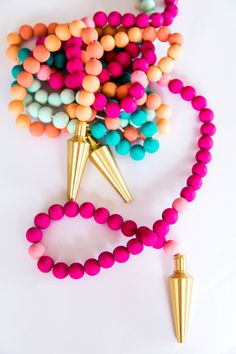 colorful beads and gold cones are on a white surface with a pink beaded necklace