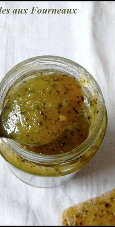 a jar filled with green sauce sitting on top of a white table cloth next to a piece of bread