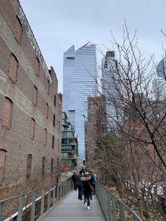 people walking on a bridge in the city with tall buildings and bare trees behind them