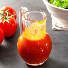 a glass measuring cup filled with liquid next to tomatoes and lettuce on a table