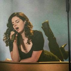 a woman sitting on top of a piano while holding a microphone in her hand and singing