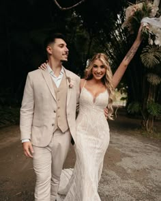 a bride and groom are walking down the road holding their arms in the air as they smile at each other