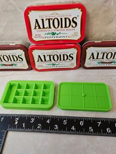 three tins of altoids sitting on top of a table next to a ruler