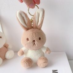 a hand holding a keychain with a stuffed animal in the shape of a bunny