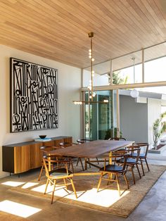 a dining room table and chairs in front of a large art piece on the wall