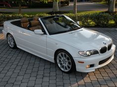 a white bmw convertible parked on top of a brick road