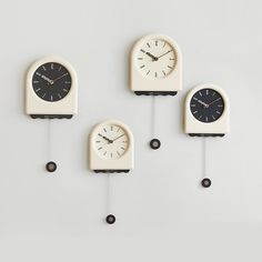 four clocks are hanging on the wall in three different shapes and sizes, one is white with black numbers