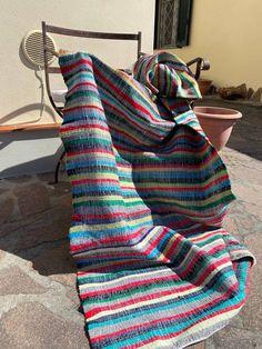 a multicolored blanket sitting on top of a wooden chair next to a potted plant