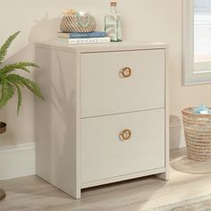 a white cabinet sitting next to a window in a room with a potted plant