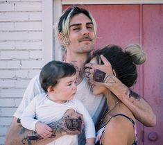 a man and woman with tattoos on their arms are holding a small child in front of a red door