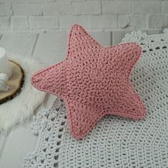 a pink crocheted star pillow sitting on top of a white blanket next to a cup