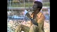 a man is sitting in the water holding a microphone and singing into it's mouth