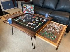 two tables with puzzles on them in front of a black couch and coffee table