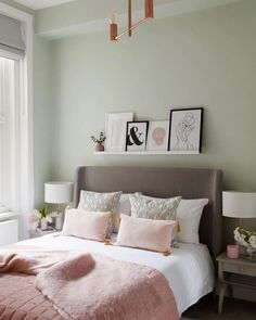 a bed in a bedroom with pink pillows and blankets on the headboard, two framed pictures above it