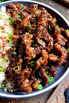 a blue plate topped with meat and rice on top of a wooden table next to chopsticks