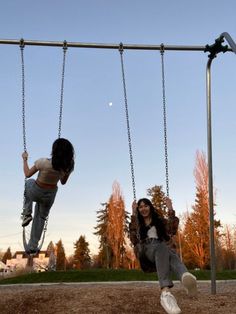 two children are playing on swings in the park