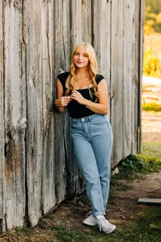 a woman leaning against a wooden wall with her hands in her pockets and looking at the camera