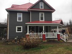 a gray house with red tin roof and white railings on the front porch area