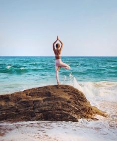 a woman standing on top of a rock in front of the ocean with her arms up