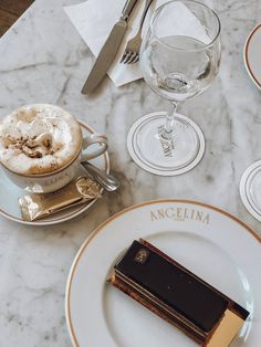 a table topped with plates and cups filled with desserts next to wine glasses on top of a marble counter