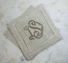 two linen napkins with the letter g on them sitting on a marble counter top