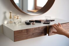 a person reaching for makeup on top of a counter next to a mirror and shelf