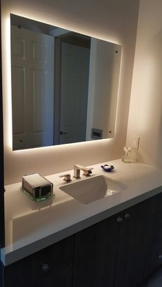 a bathroom vanity with a large mirror above it and lights on the wall behind it