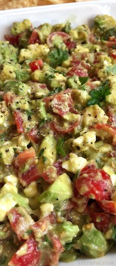 a salad with tomatoes, avocado and other toppings in a white dish