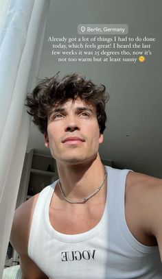 a young man wearing a white tank top standing in front of a window with his eyes closed