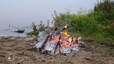 there is a fire burning in the middle of the ground next to some grass and water