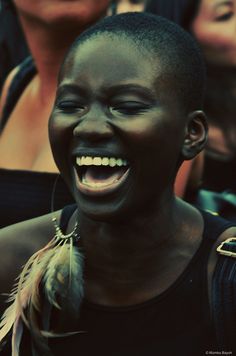 a woman laughing with her eyes closed and feathers around her neck in front of other people