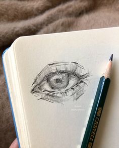 a pencil drawing of an eye on top of a book next to a brown blanket