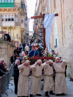 several people dressed in long robes and hats are gathered around a statue on a city street