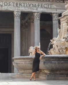 a woman standing in front of a fountain with her hand on her hip and looking at the camera