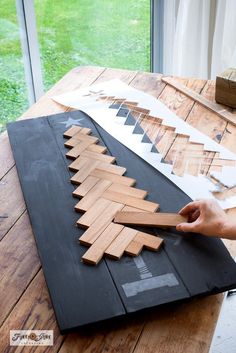 someone is making a christmas tree out of wood planks on a table in front of a window